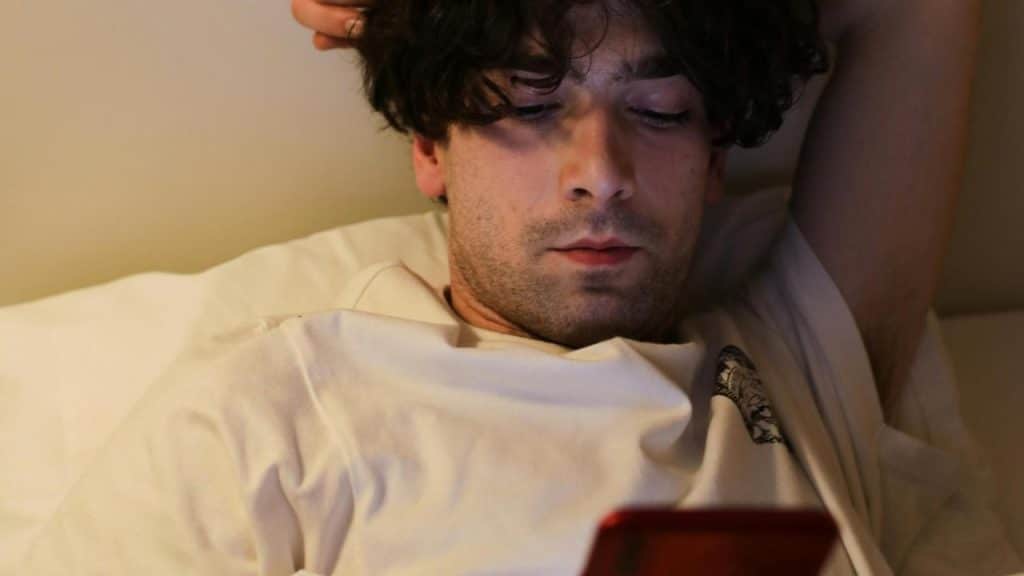 A man lies in bed while looking at his phone.