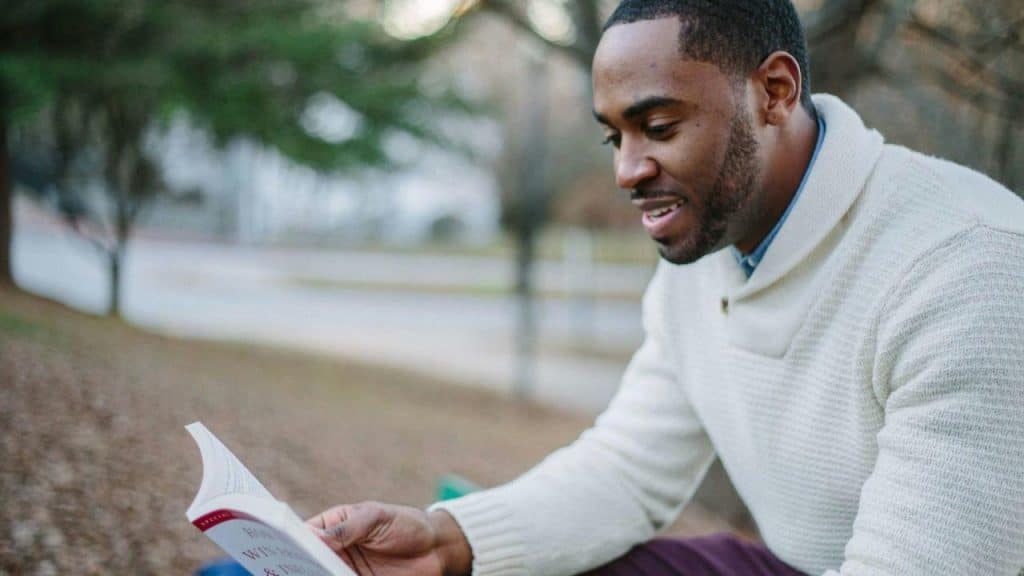 A man sits outdoors reading a book.