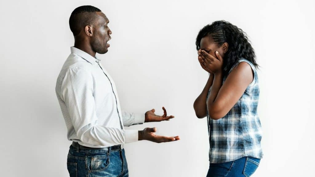 A man talks with open hands toward a woman covering her face with both hands.