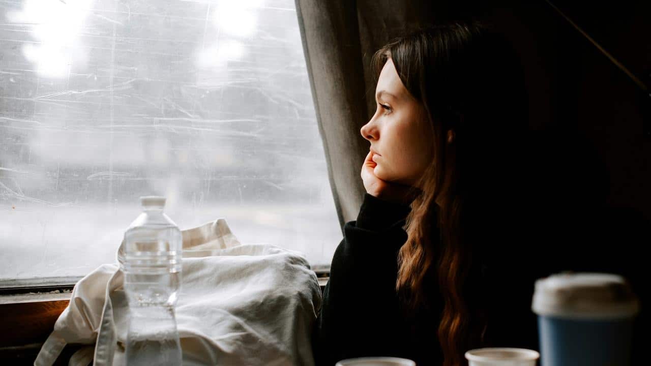 A woman gazes out a window while resting her chin on her hand