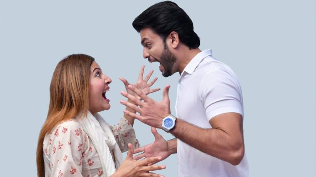 A man and woman stand facing each other with mouths open and hands raised.