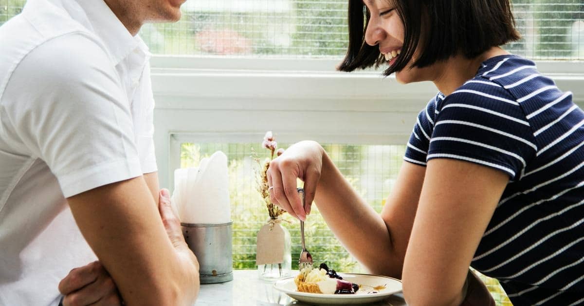 A couple smiling while sharing dessert at a café table