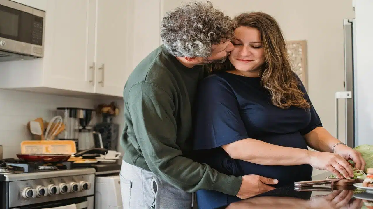 A man kissing his wife in the kitchen