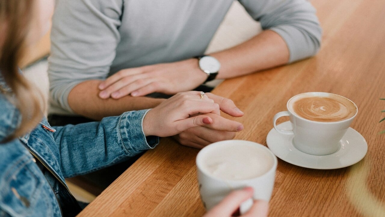 A man and a woman holding hands while having coffee