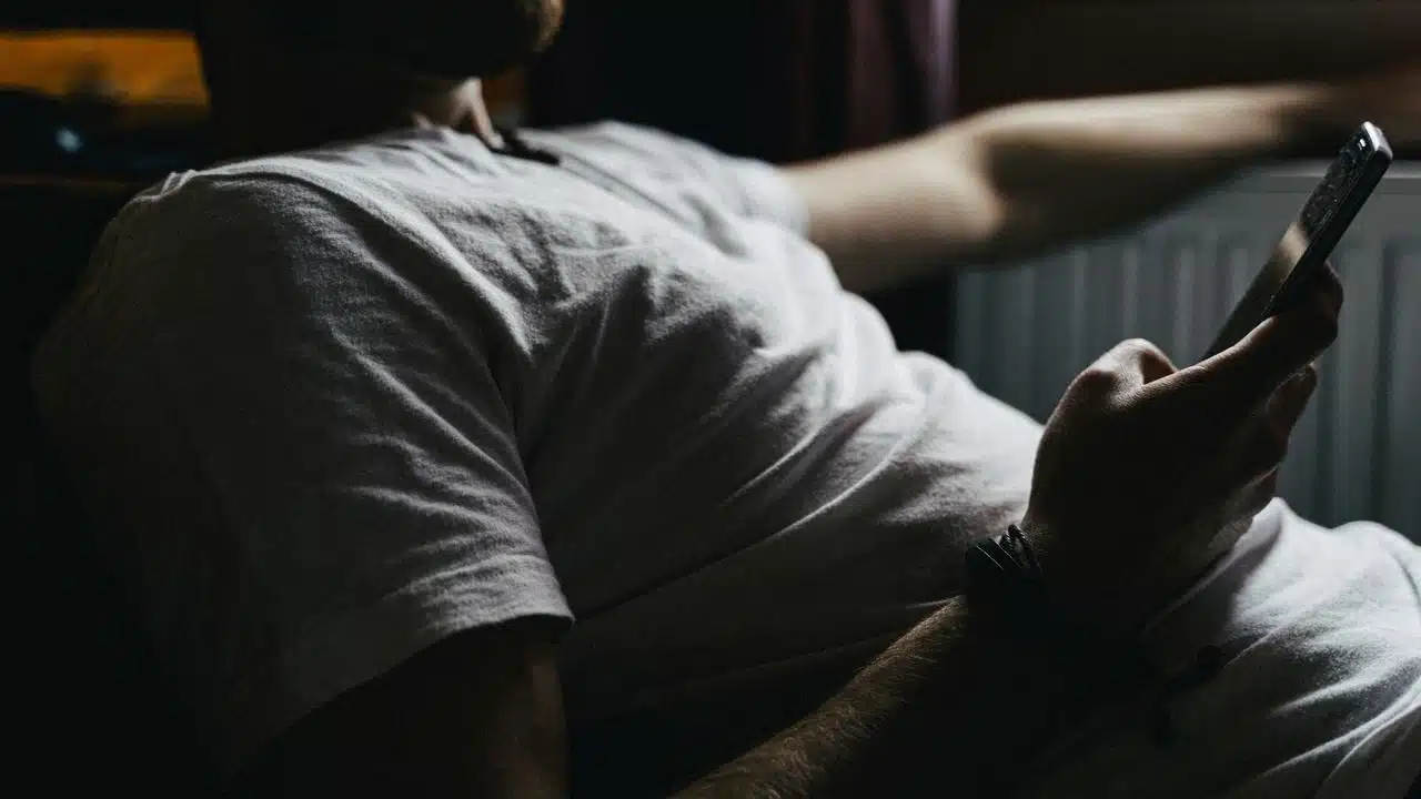 A person in a white t-shirt reclines while holding a smartphone