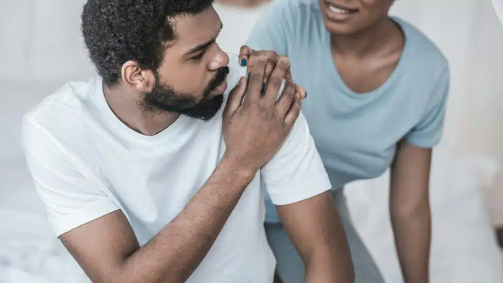 A worried man sits while a woman comforts him