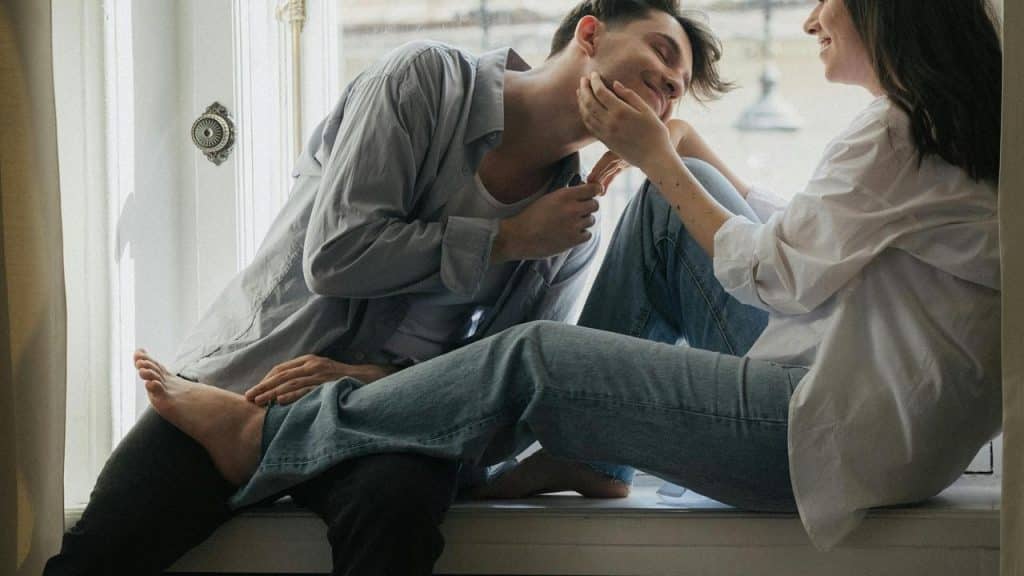 A couple sitting by a window sharing a playful, affectionate moment.