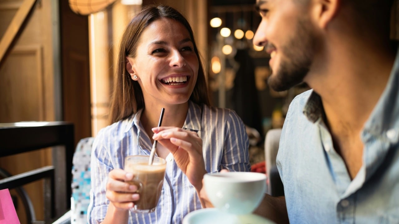 A woman in a striped shirt laughs while holding a drink across from a man.