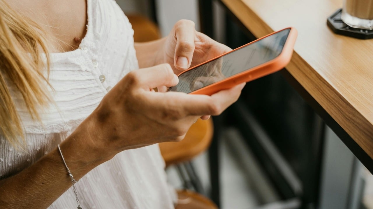 A close-up view of a person's hands typing on a smartphone with an orange case.