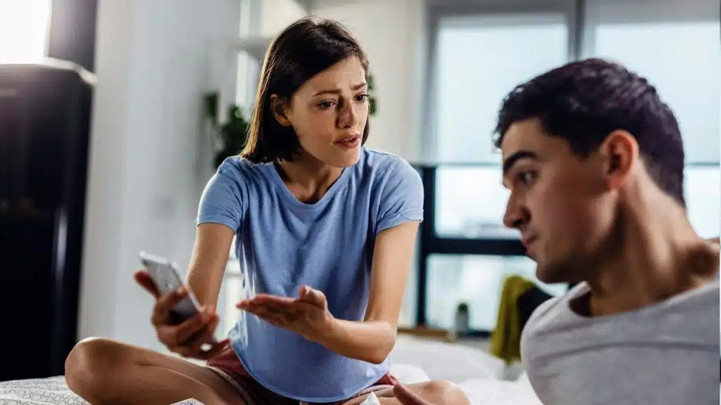 Disappointed woman arguing with her boyfriend about a text message on her mobile phone.