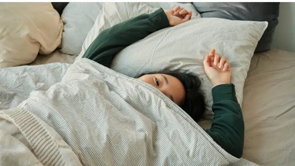 a woman lying in bed under a blanket.
