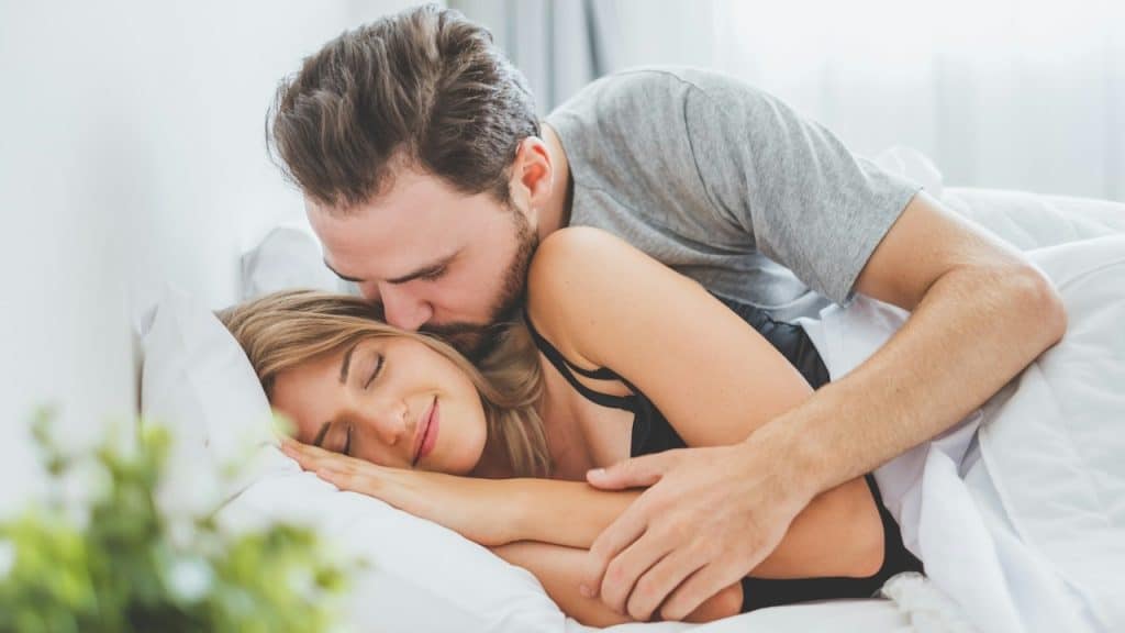 Man kissing his wife while she is sleeping, facing opposite to him.