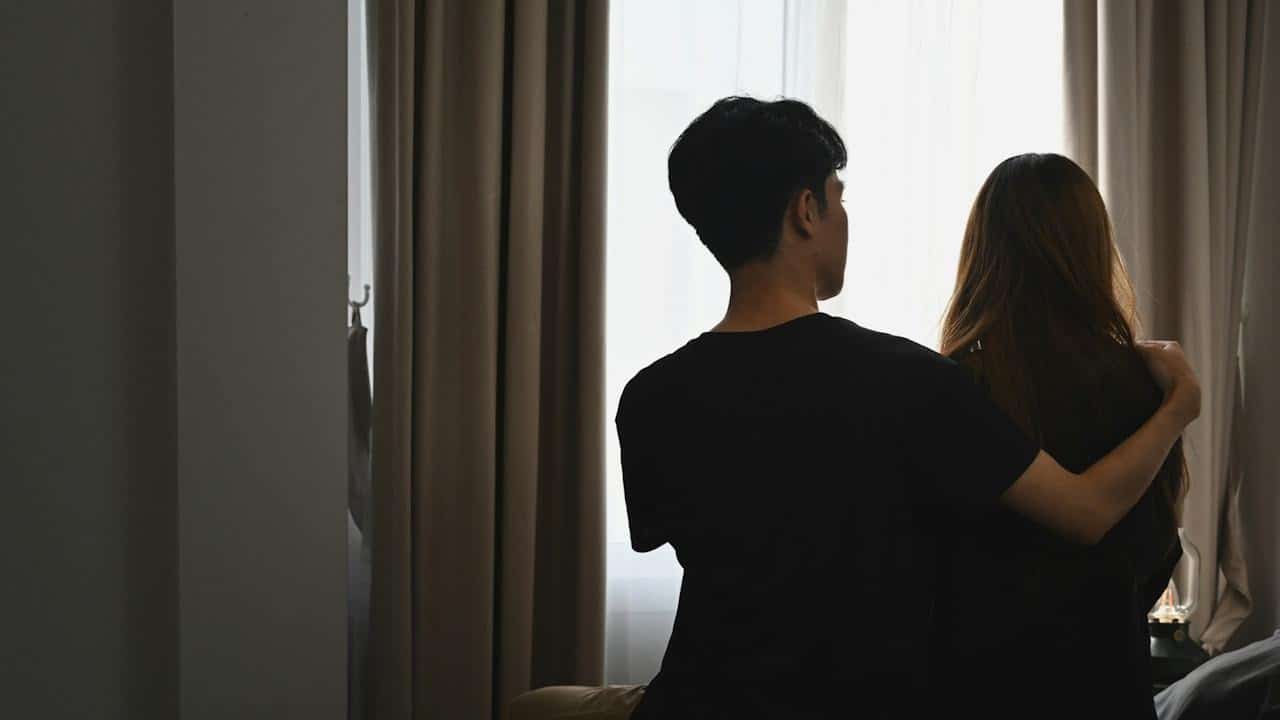 A young man is embracing his girlfriend and sitting in the bedroom.