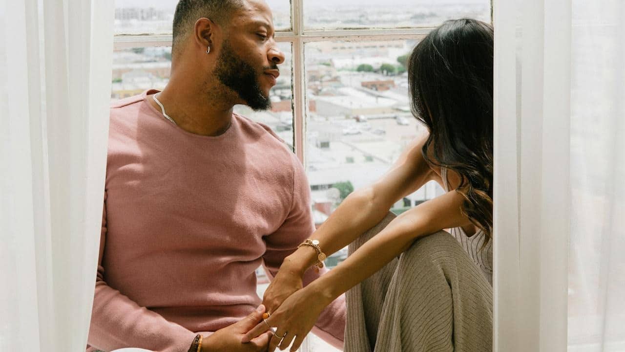 A man and a woman are sitting on a windowsill.