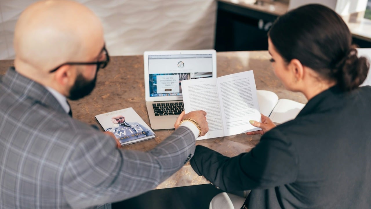 A man and a woman reading some documents while sitting at a table.