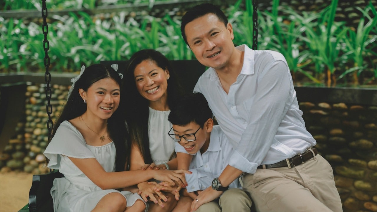 A happy family of four sitting on a swing outdoors.