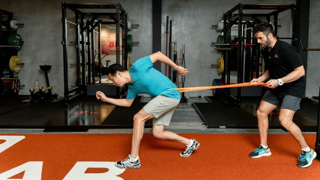A man in a blue shirt performs a resisted sprint exercise with a fitness trainer.