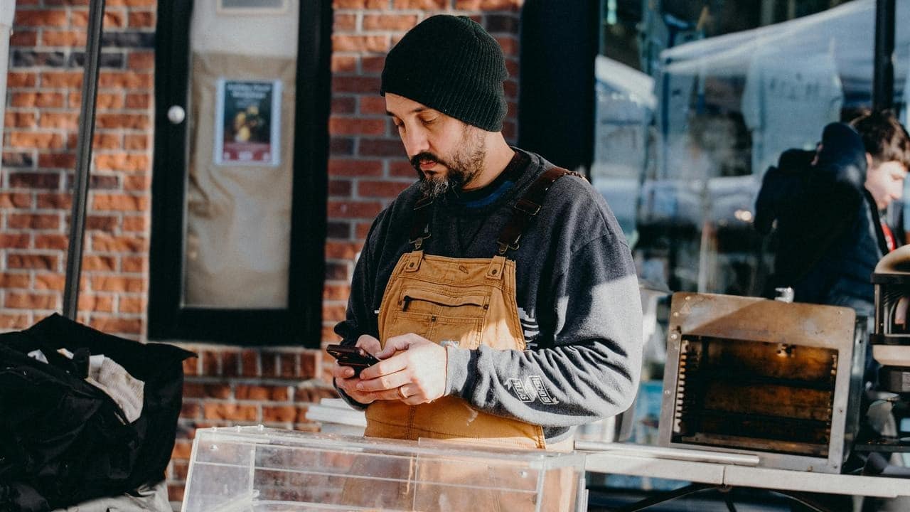 A man wearing an apron checks his phone while working.