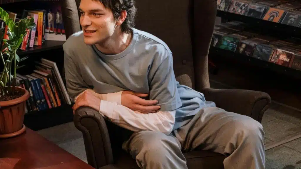 A man sits in a chair smiling while talking indoors.
