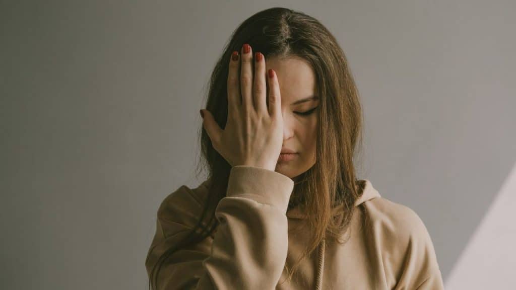 A woman with red-painted nails is covering her face with one hand.