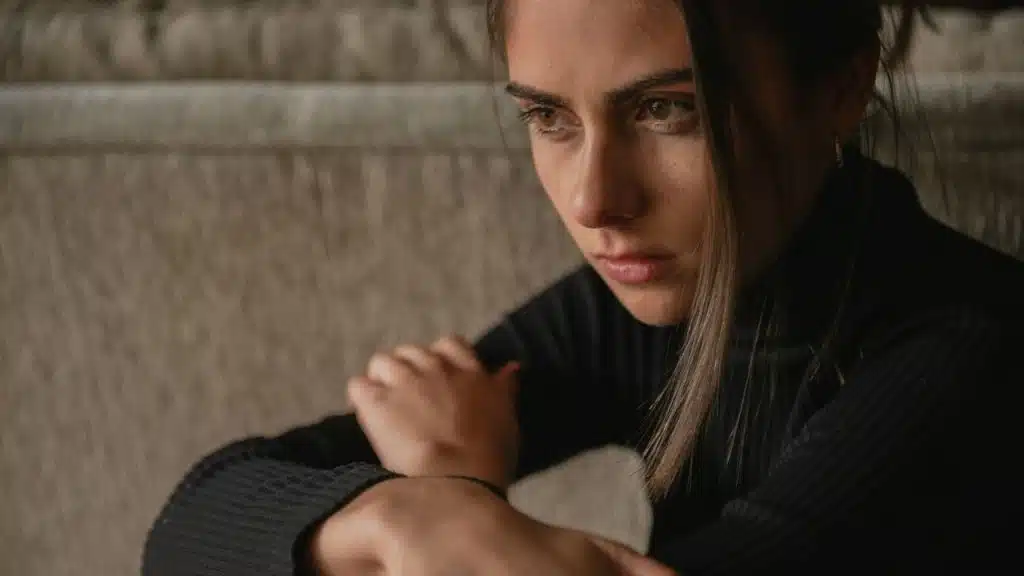 A sad woman is looking down, with her hands clasped together.