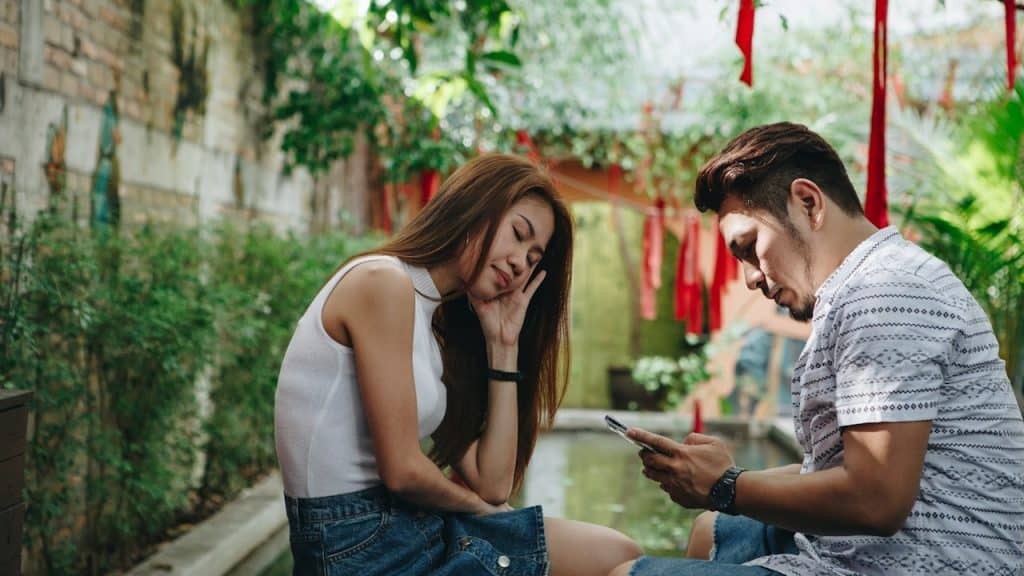 A man is using cellphone while his frustrated wife is sitting next to him.