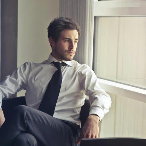 A man in a white shirt and tie sitting by a window