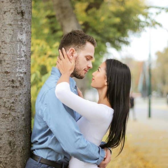 A couple standing close together by a tree