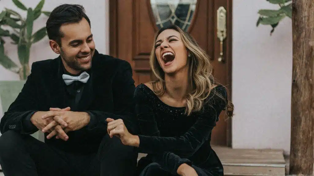 A man and a woman laughing while sitting outside their house.