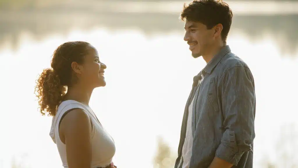 Smiling man and woman engaged in a conversation with a body of water in the background.