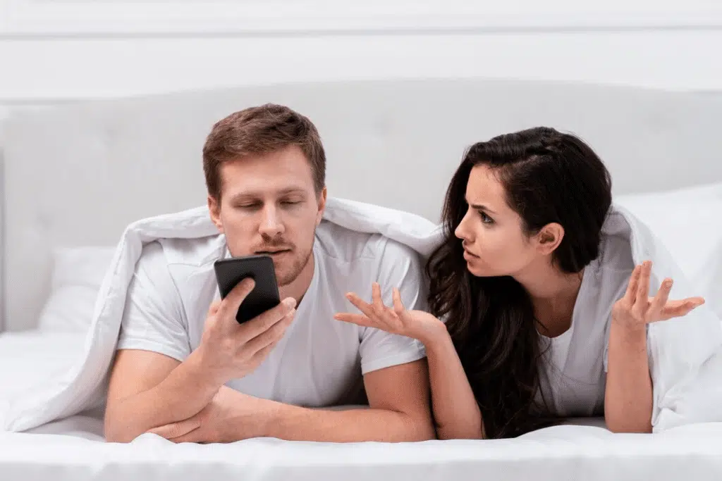 Man ignoring wife while on phone in bed