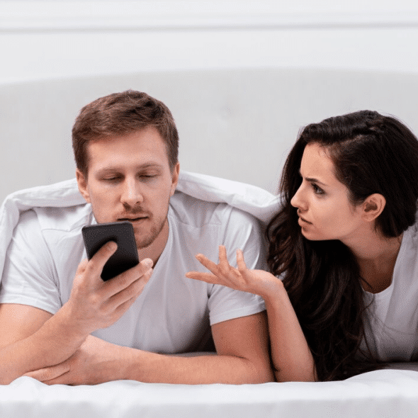 Man ignoring wife while on phone in bed