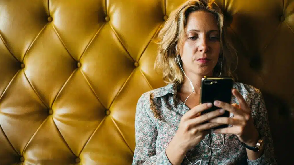 A woman wearing earphones looking at her smartphone.