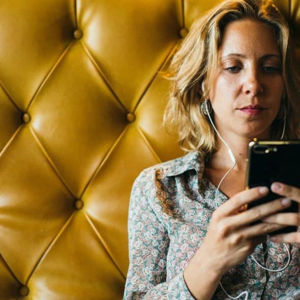 A woman wearing earphones looking at her smartphone.
