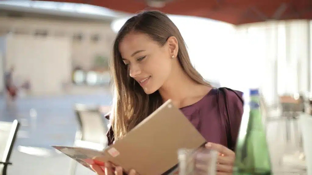 A woman sitting at an outdoor café table and reading a menu.