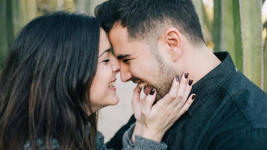 A smiling couple touching foreheads while holding each other’s faces.