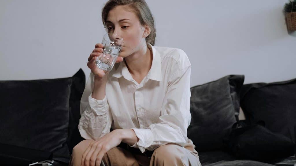 A woman sitting on a couch drinking a glass of water.