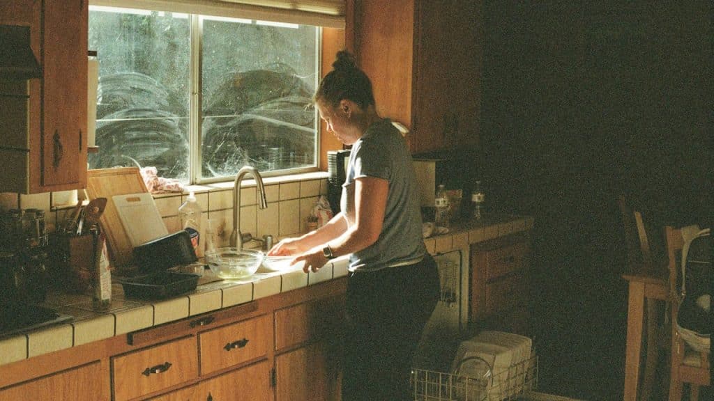 A woman working in the kitchen and washing dishes in the sink.