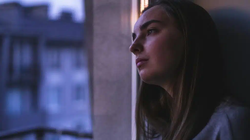 A woman gazing out a window with a thoughtful expression.