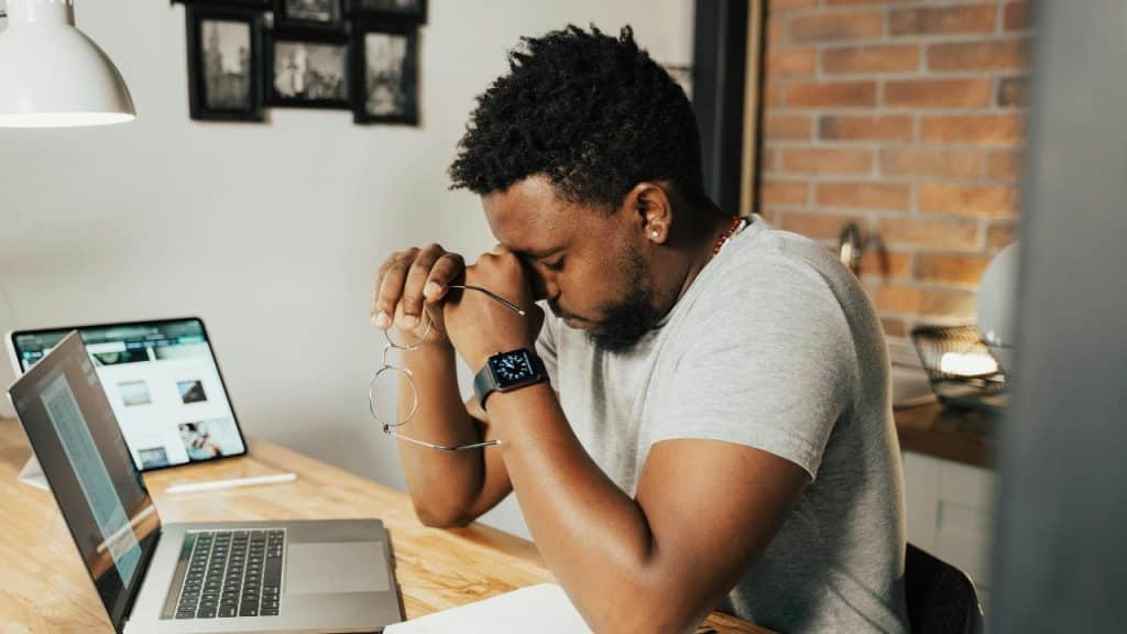 A person sits at a desk with their head in hands, looking down at papers.