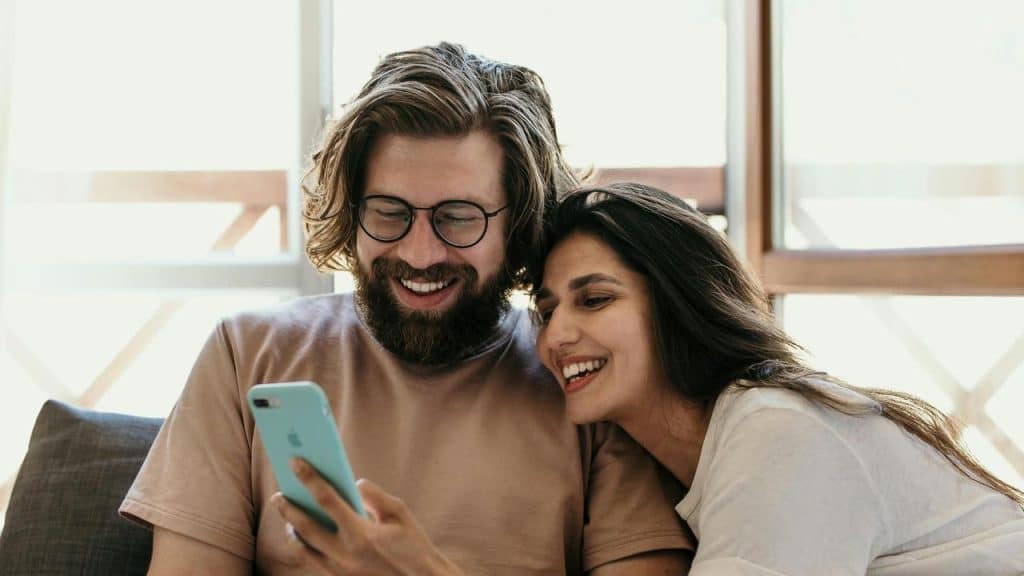 A smiling couple sitting together and looking at a smartphone.