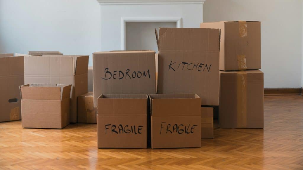 Several cardboard moving boxes labeled Bedroom, Kitchen, and Fragile sit on a wooden floor.