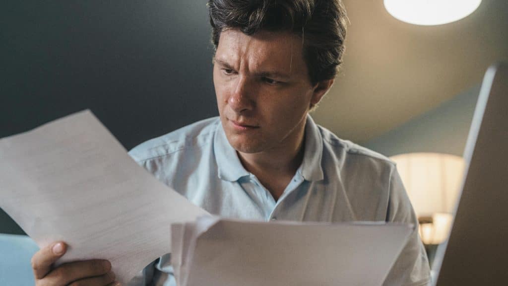 A man looks intently at a document he is holding in a dimly lit room.