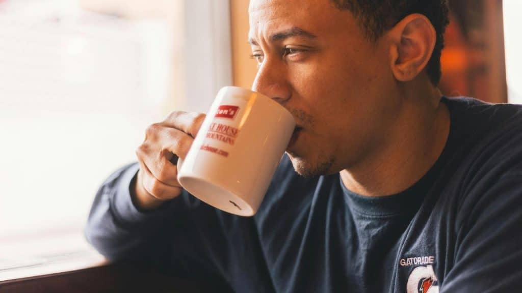 A man drinking from a coffee mug while looking out a window.