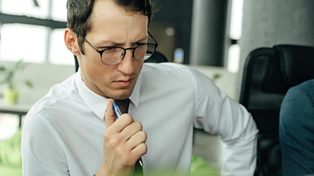 A man in glasses holding a pen and looking concerned.
