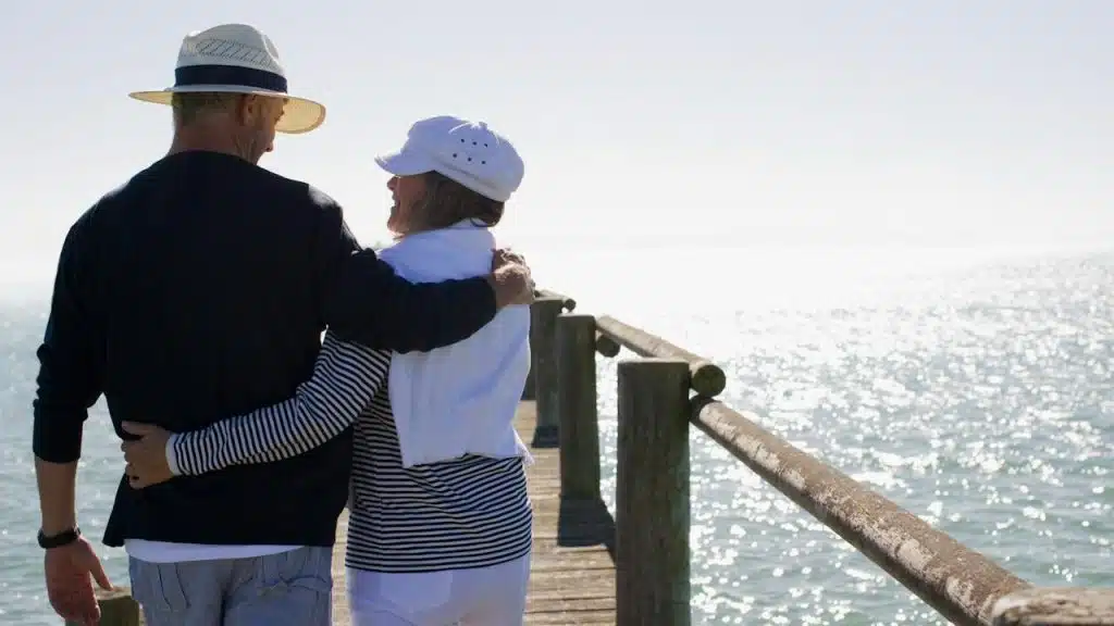 A couple walking down a pier with their arms around each other.