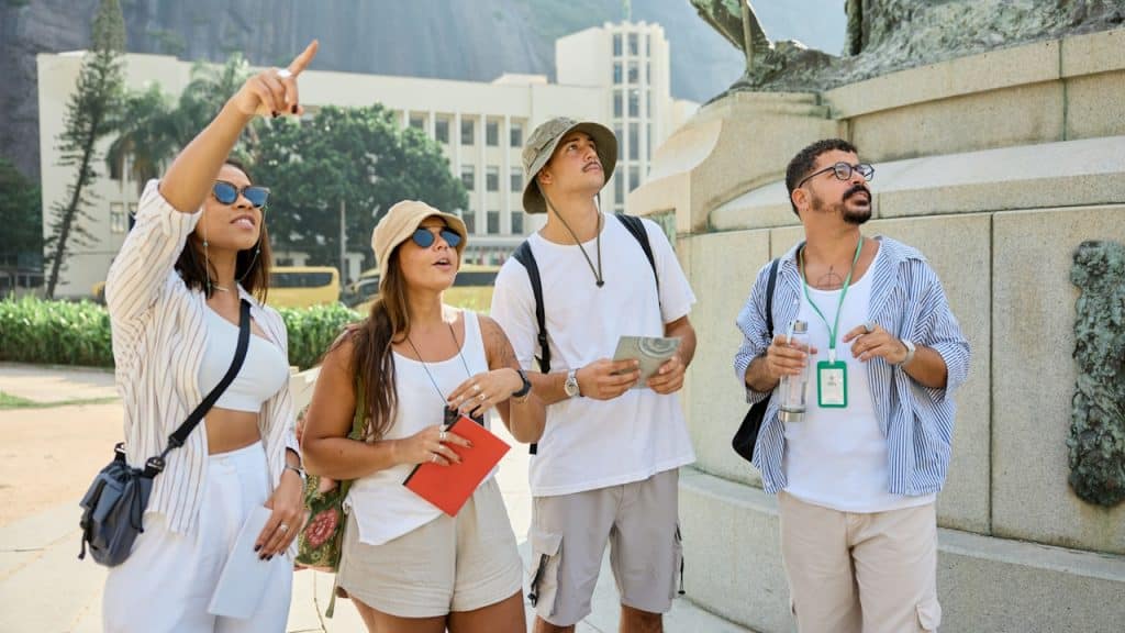 A group of people standing next to a statue while one woman points upwards with her finger and the rest look at where she’s pointing.
