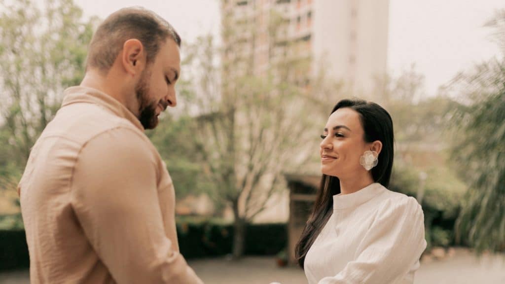 A man in a tan shirt and a woman in white look at each other.