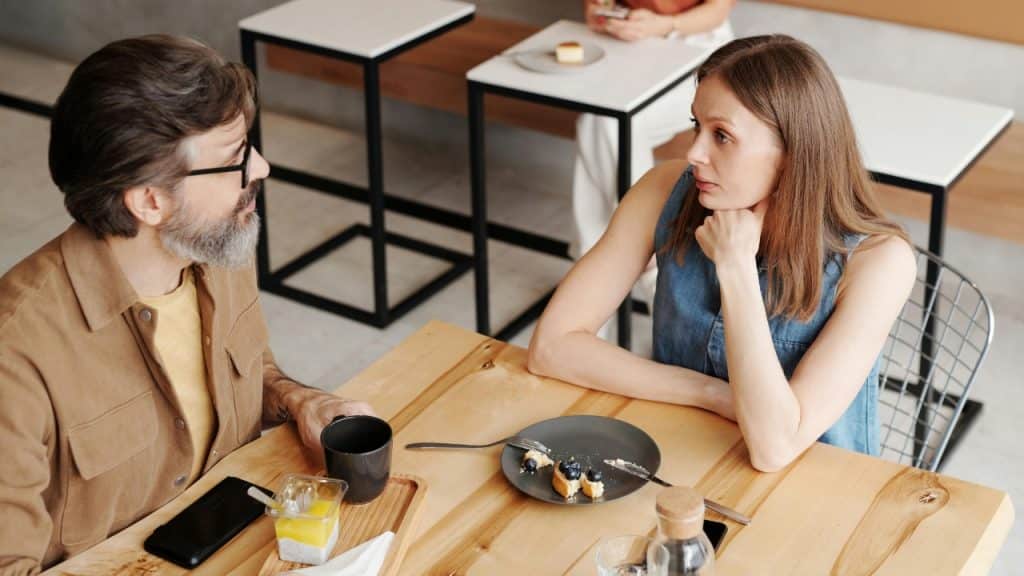 A man and woman sit at a wooden table in a cafe talking together.