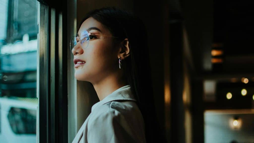 A woman wearing glasses looking out a window.